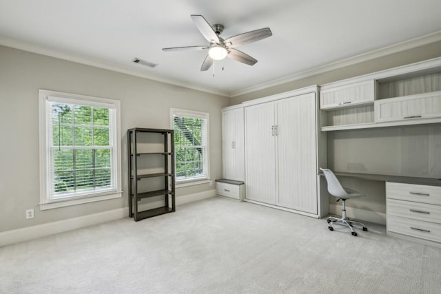 unfurnished office with a ceiling fan, healthy amount of natural light, crown molding, light colored carpet, and built in desk