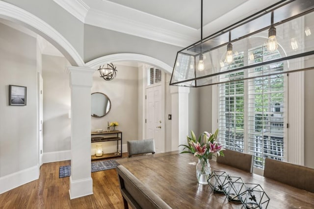 dining area with arched walkways, ornate columns, crown molding, wood finished floors, and baseboards