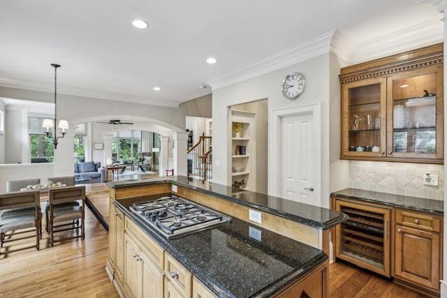 kitchen with stainless steel gas stovetop, beverage cooler, arched walkways, crown molding, and a center island