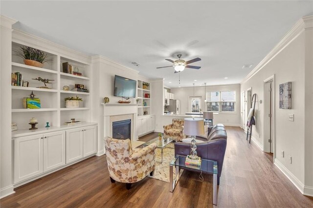 living room with hardwood / wood-style flooring, crown molding, built in features, and ceiling fan