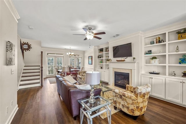 living room with crown molding, dark hardwood / wood-style floors, ceiling fan with notable chandelier, and built in features