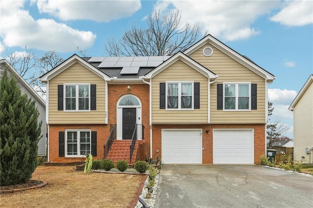 raised ranch with brick siding, solar panels, driveway, and an attached garage