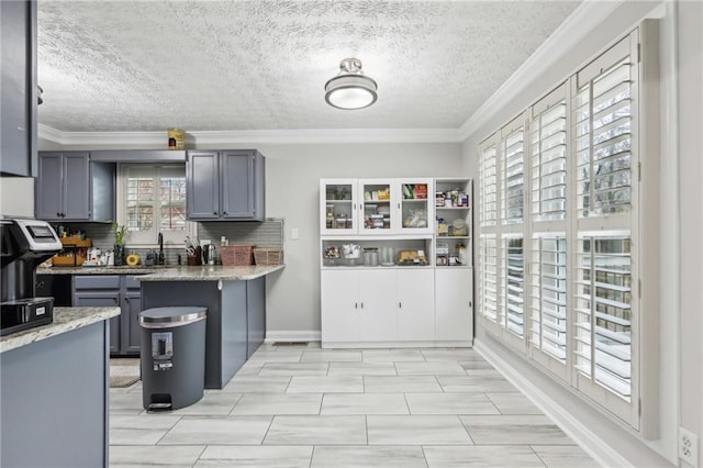 kitchen featuring light stone counters, backsplash, gray cabinetry, and ornamental molding