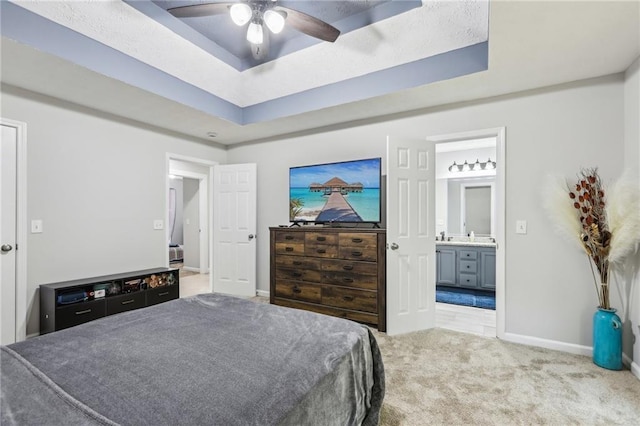 carpeted bedroom featuring a raised ceiling, baseboards, ensuite bathroom, and ceiling fan