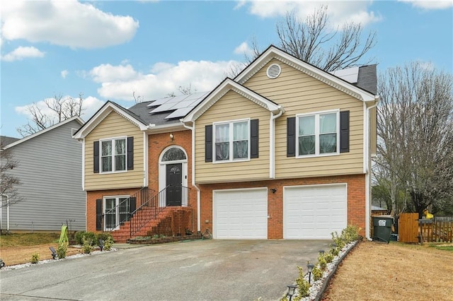 split foyer home featuring aphalt driveway, roof mounted solar panels, fence, an attached garage, and brick siding