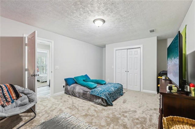 carpeted bedroom featuring a textured ceiling, visible vents, a closet, and baseboards