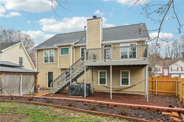 back of house featuring a deck, fence, stairway, a shingled roof, and a chimney