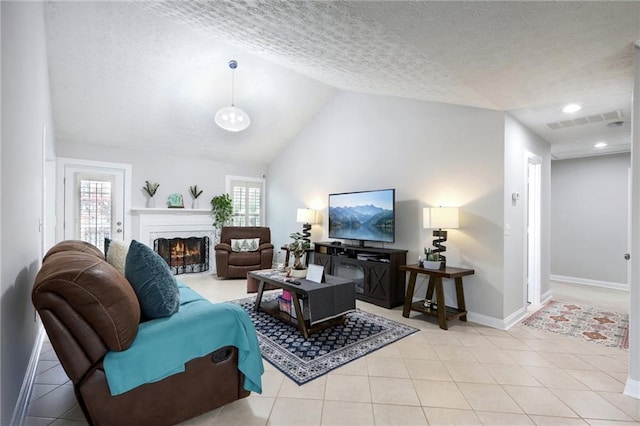 living area featuring a textured ceiling, light tile patterned floors, visible vents, and a lit fireplace