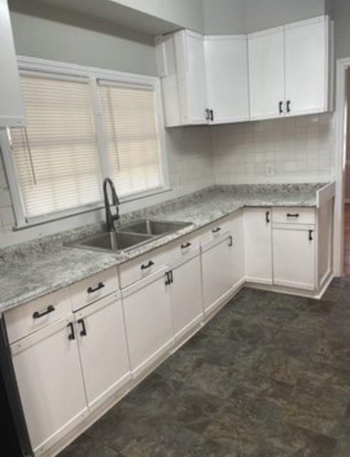 kitchen with light stone counters, sink, tasteful backsplash, and white cabinets