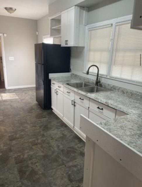 kitchen with white cabinetry, sink, black refrigerator, and light stone countertops