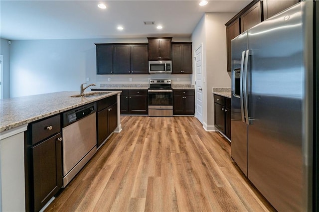 kitchen with light stone counters, dark brown cabinets, stainless steel appliances, sink, and light hardwood / wood-style floors