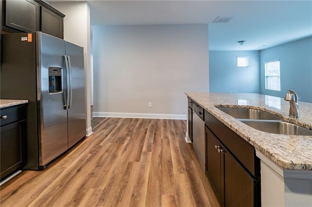 kitchen with light stone countertops, appliances with stainless steel finishes, dark brown cabinets, sink, and hardwood / wood-style flooring