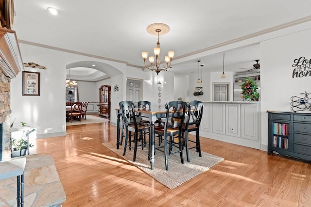 dining area featuring ornamental molding, a tray ceiling, ceiling fan with notable chandelier, and light hardwood / wood-style flooring