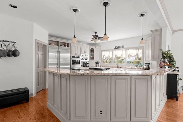 kitchen featuring pendant lighting, stainless steel appliances, light stone countertops, and light wood-type flooring