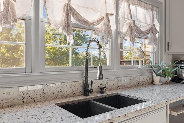 room details featuring white cabinetry, light stone countertops, and sink