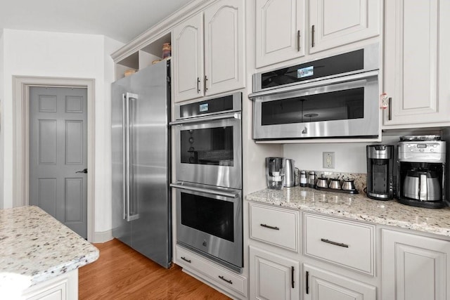 kitchen with light stone counters, stainless steel appliances, light hardwood / wood-style floors, and white cabinets