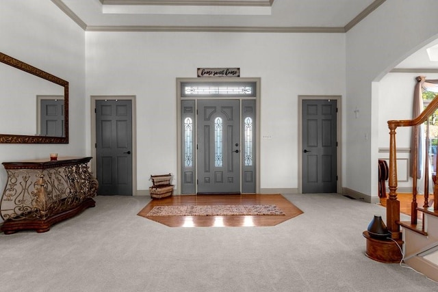 carpeted foyer with ornamental molding, a raised ceiling, and a high ceiling