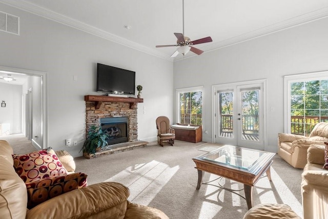 carpeted living room featuring a stone fireplace, plenty of natural light, ornamental molding, and french doors