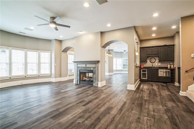 unfurnished living room featuring dark hardwood / wood-style flooring, wine cooler, ceiling fan, and a multi sided fireplace