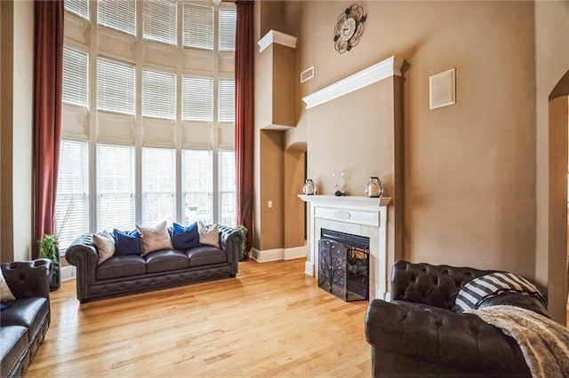 living room featuring a fireplace, light hardwood / wood-style floors, and a high ceiling