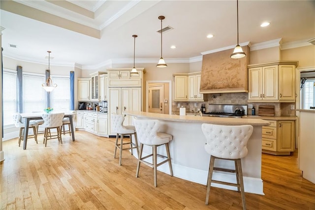 kitchen featuring a kitchen bar, hanging light fixtures, light wood-type flooring, a center island with sink, and backsplash