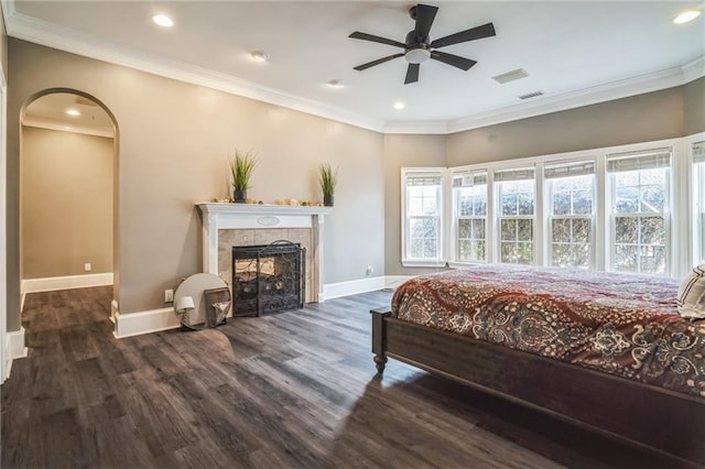 bedroom with a tiled fireplace, crown molding, dark hardwood / wood-style floors, and ceiling fan