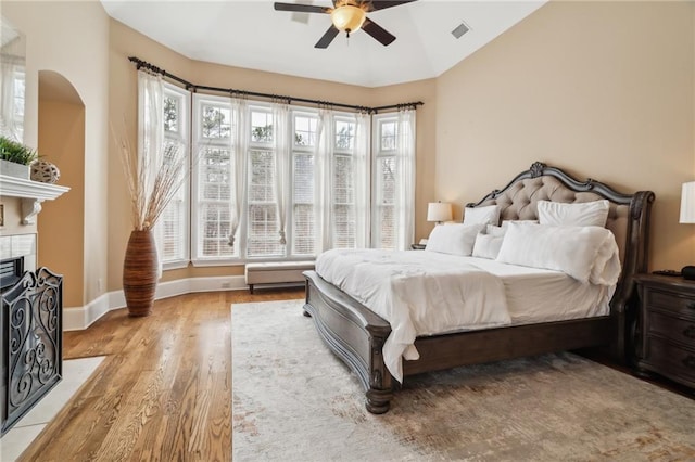 bedroom featuring a tiled fireplace, vaulted ceiling, ceiling fan, and light hardwood / wood-style floors