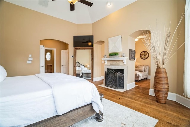 bedroom featuring ceiling fan, hardwood / wood-style floors, a fireplace, and high vaulted ceiling