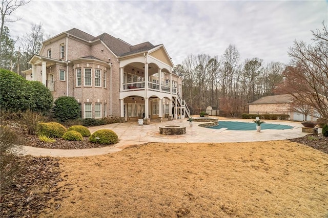 rear view of property featuring a fire pit, a patio area, a balcony, and a covered pool