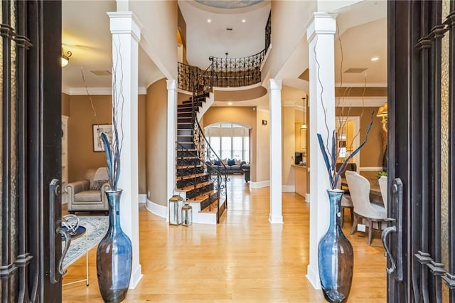 foyer featuring a towering ceiling, ornamental molding, hardwood / wood-style floors, and ornate columns