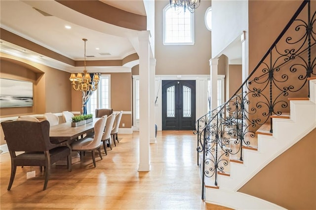 entryway featuring decorative columns, a notable chandelier, ornamental molding, light hardwood / wood-style floors, and french doors