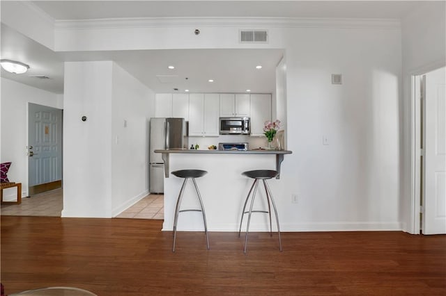 kitchen with light wood-type flooring, kitchen peninsula, a kitchen breakfast bar, stainless steel appliances, and white cabinets