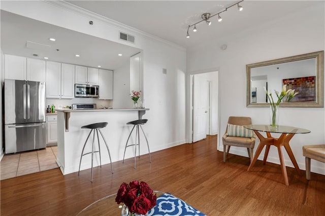 kitchen featuring a breakfast bar, white cabinets, stainless steel appliances, and light wood-type flooring