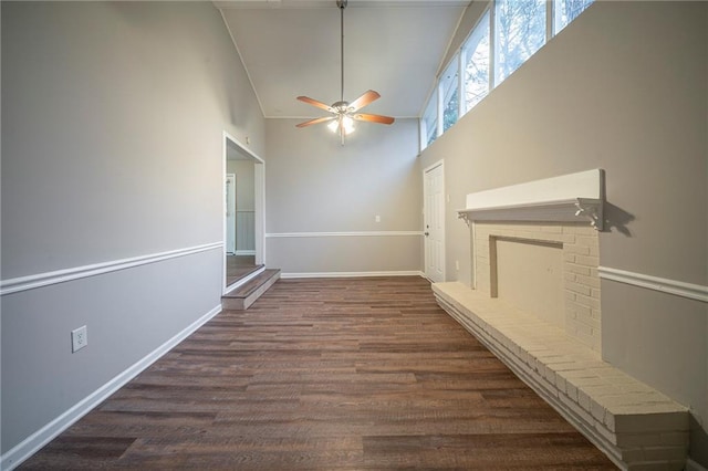 interior space with ceiling fan, dark hardwood / wood-style flooring, a brick fireplace, and a towering ceiling