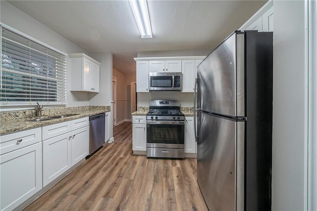 kitchen with sink, white cabinetry, light stone counters, appliances with stainless steel finishes, and hardwood / wood-style floors