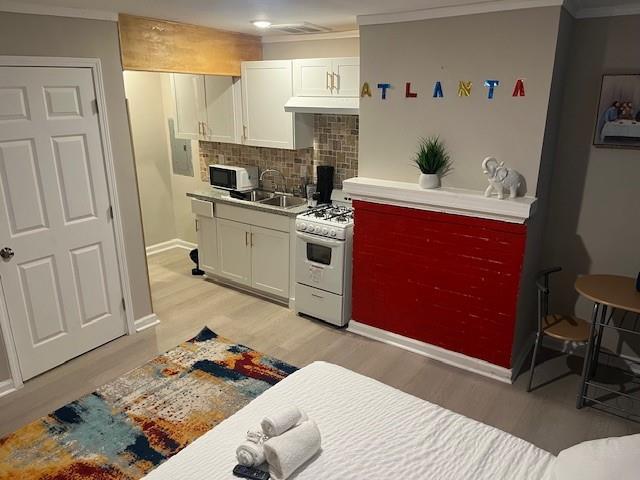10 Rockmart Dr NW, Atlanta, GA 30314 - kitchen with white appliances, light wood finished floors, ornamental molding, white cabinets, and tasteful backsplash