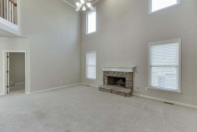 unfurnished living room with ceiling fan, a stone fireplace, light colored carpet, and a towering ceiling