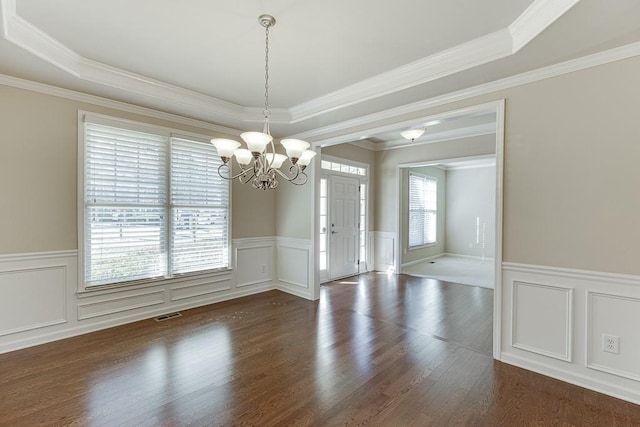 unfurnished dining area with a tray ceiling, crown molding, dark hardwood / wood-style floors, and an inviting chandelier