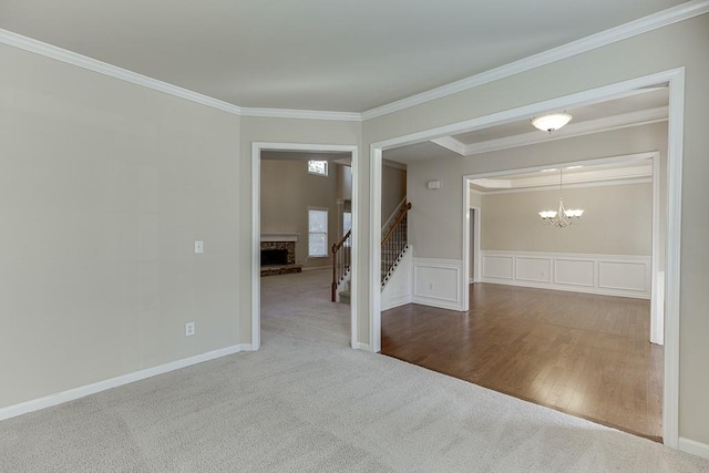 unfurnished room featuring a stone fireplace, hardwood / wood-style floors, an inviting chandelier, and ornamental molding