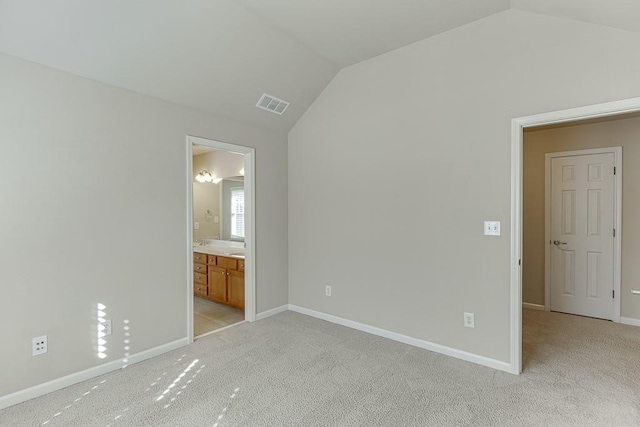 unfurnished bedroom featuring ensuite bathroom, light colored carpet, and lofted ceiling