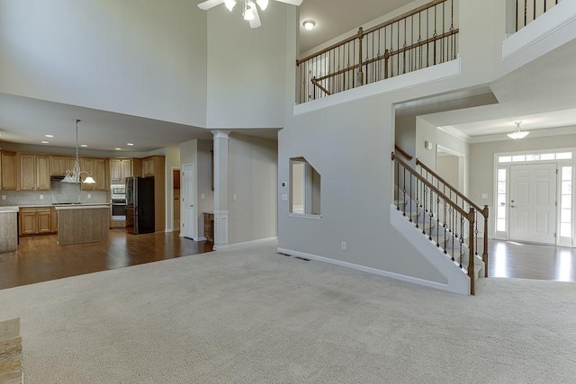 unfurnished living room with ornate columns, a towering ceiling, light colored carpet, and ornamental molding