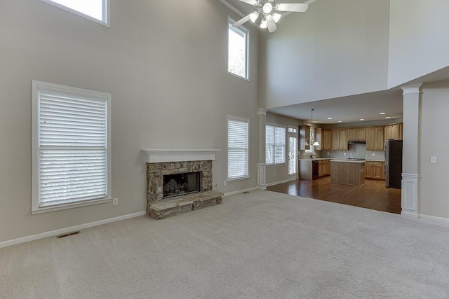 unfurnished living room with carpet, a stone fireplace, ceiling fan, and a towering ceiling