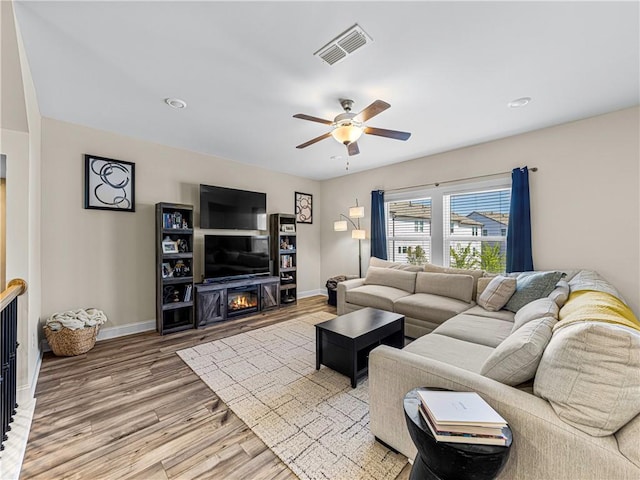 living area with light wood-style floors, ceiling fan, a lit fireplace, baseboards, and visible vents