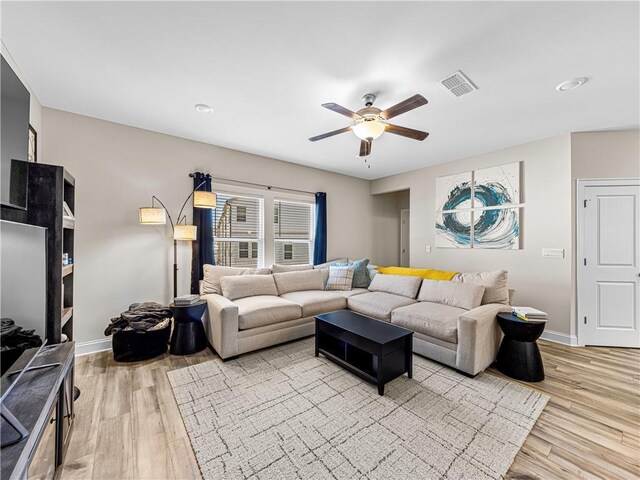 living room with light wood-style floors, visible vents, baseboards, and ceiling fan