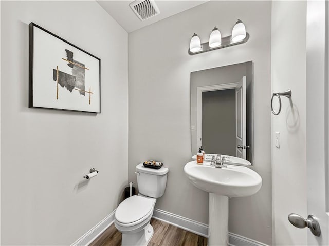 bathroom featuring toilet, wood finished floors, a sink, baseboards, and visible vents