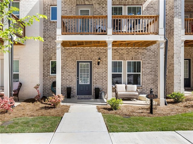view of exterior entry featuring brick siding and a balcony