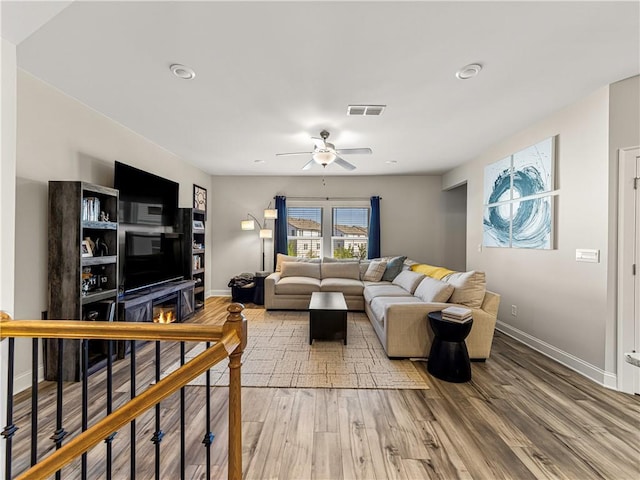 living area featuring light wood-type flooring, visible vents, a ceiling fan, and baseboards
