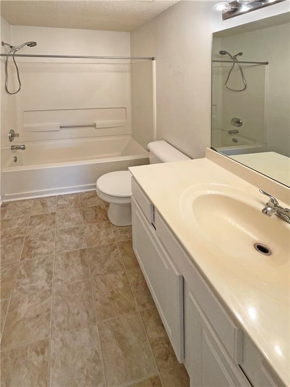 bathroom with  shower combination, a textured ceiling, toilet, and vanity