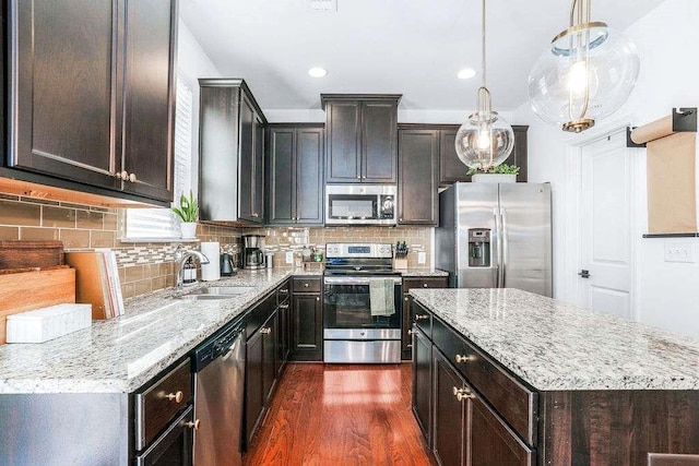 kitchen featuring sink, light stone counters, pendant lighting, stainless steel appliances, and backsplash