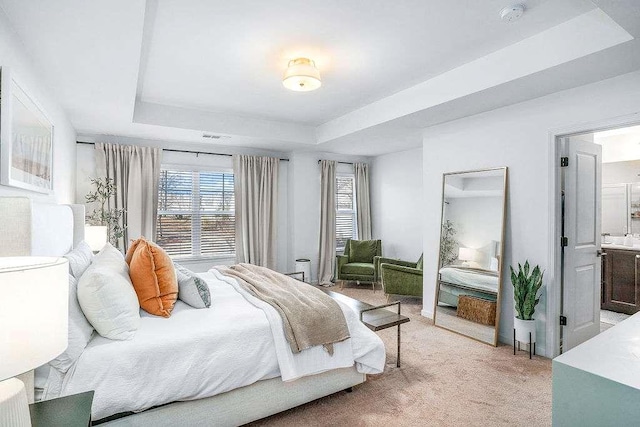 bedroom featuring ensuite bathroom, light colored carpet, and a tray ceiling